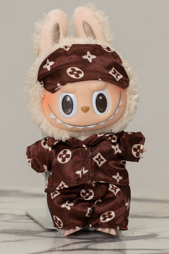 A plush, smiling rabbit-like doll wearing a brown and white patterned pajama set with a matching headband.