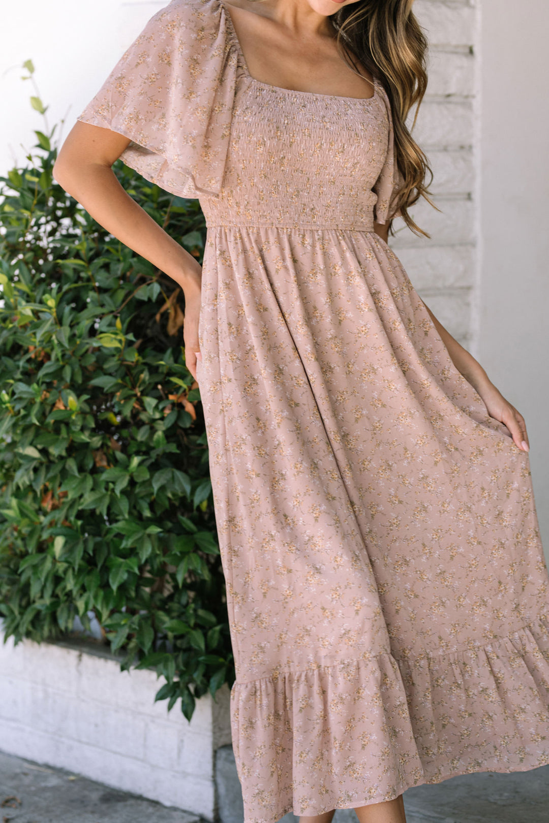 Flowing midi dress in a soft blush floral print, featuring a smocked bodice and fluttery sleeves for a romantic, feminine style.