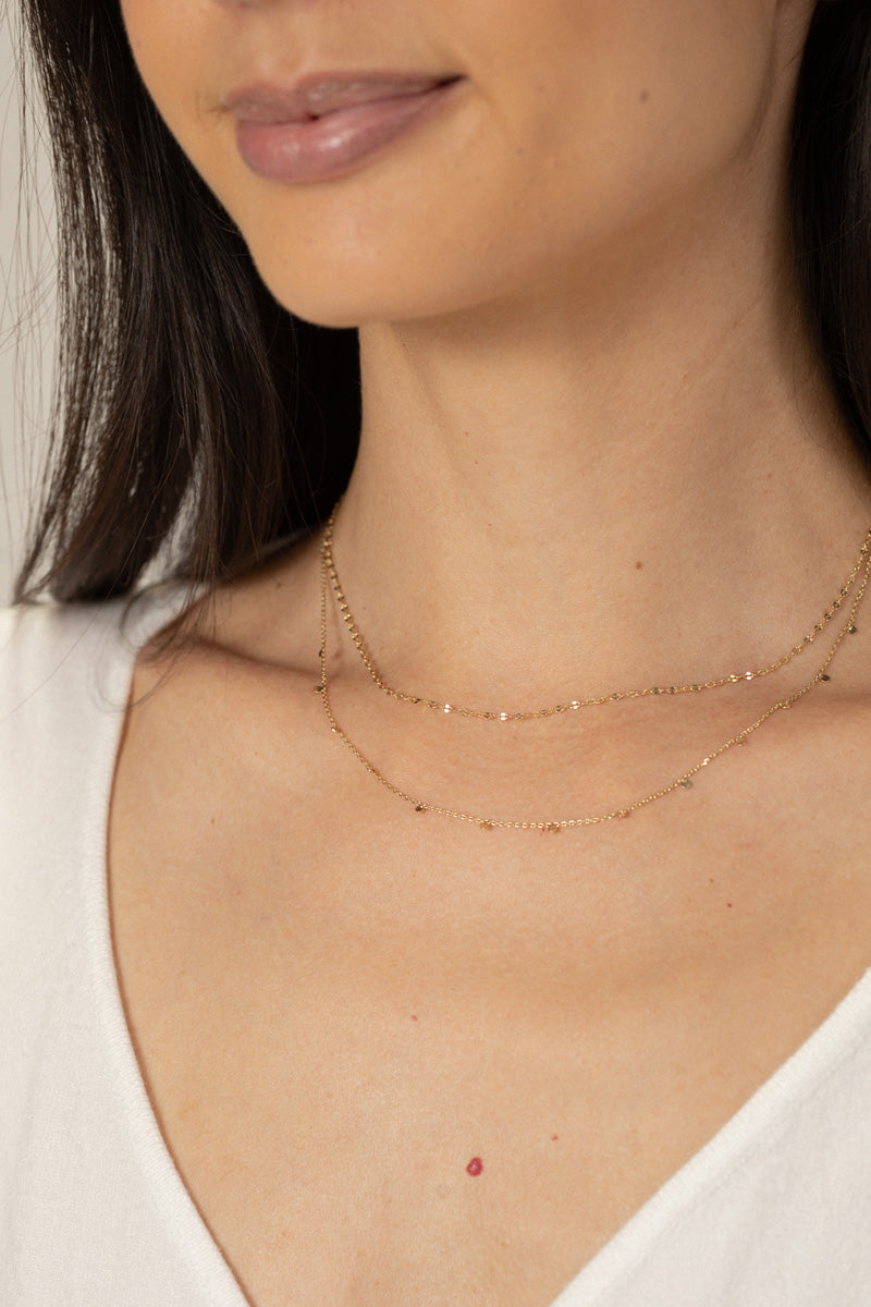 Close-up of a delicate, multi-layered gold chain necklace with a small metal bead detail, against a white background.