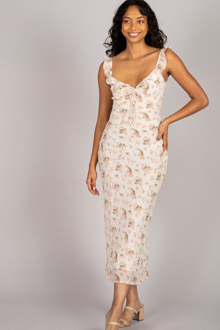 A floral chiffon dress with a V-neck, ruffled straps, and a midi-length hemline, worn by a smiling woman with curly dark hair.