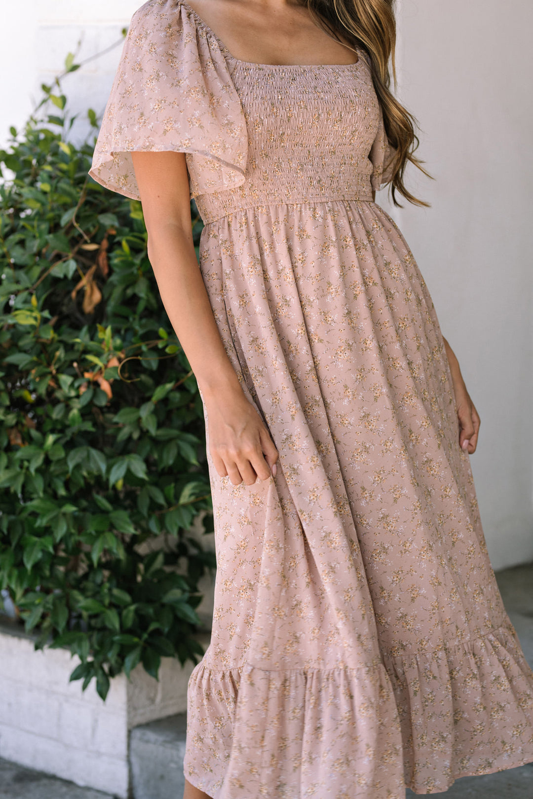 A midi-length floral dress in a dusty pink hue, featuring a smocked bodice, puff sleeves, and a tiered, flowing skirt.