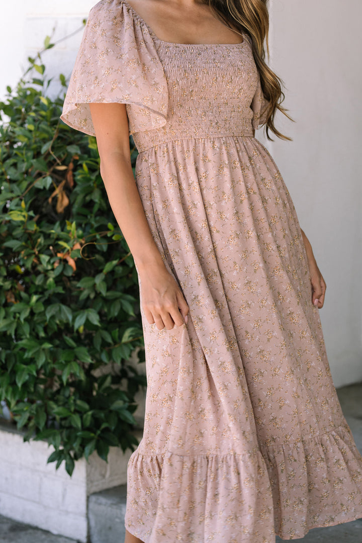 A midi-length floral dress in a dusty pink hue, featuring a smocked bodice, puff sleeves, and a tiered, flowing skirt.