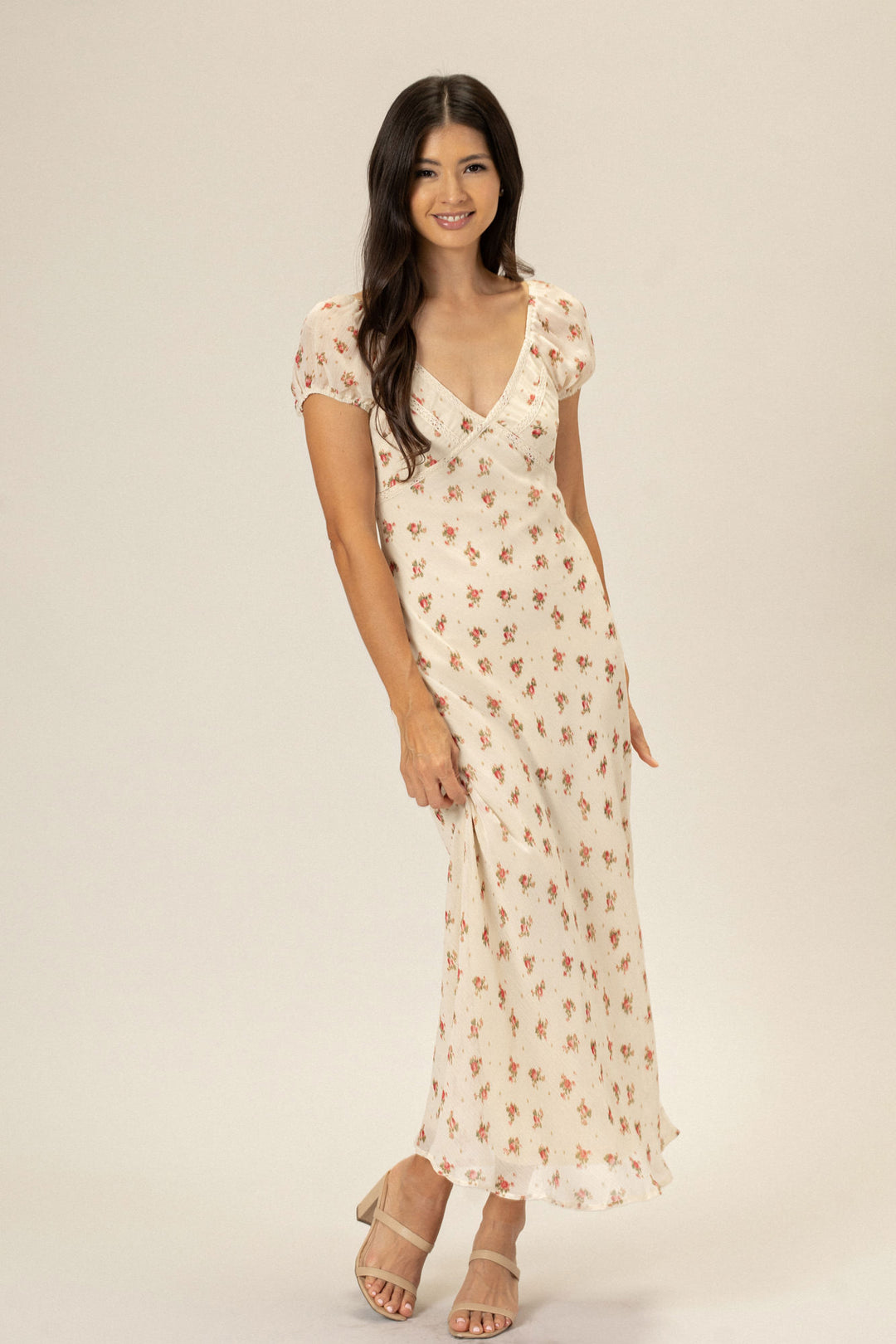 A floral-printed, v-neck dress with short puff sleeves and a flowy, ankle-length skirt, modeled by a smiling woman with long brown hair.