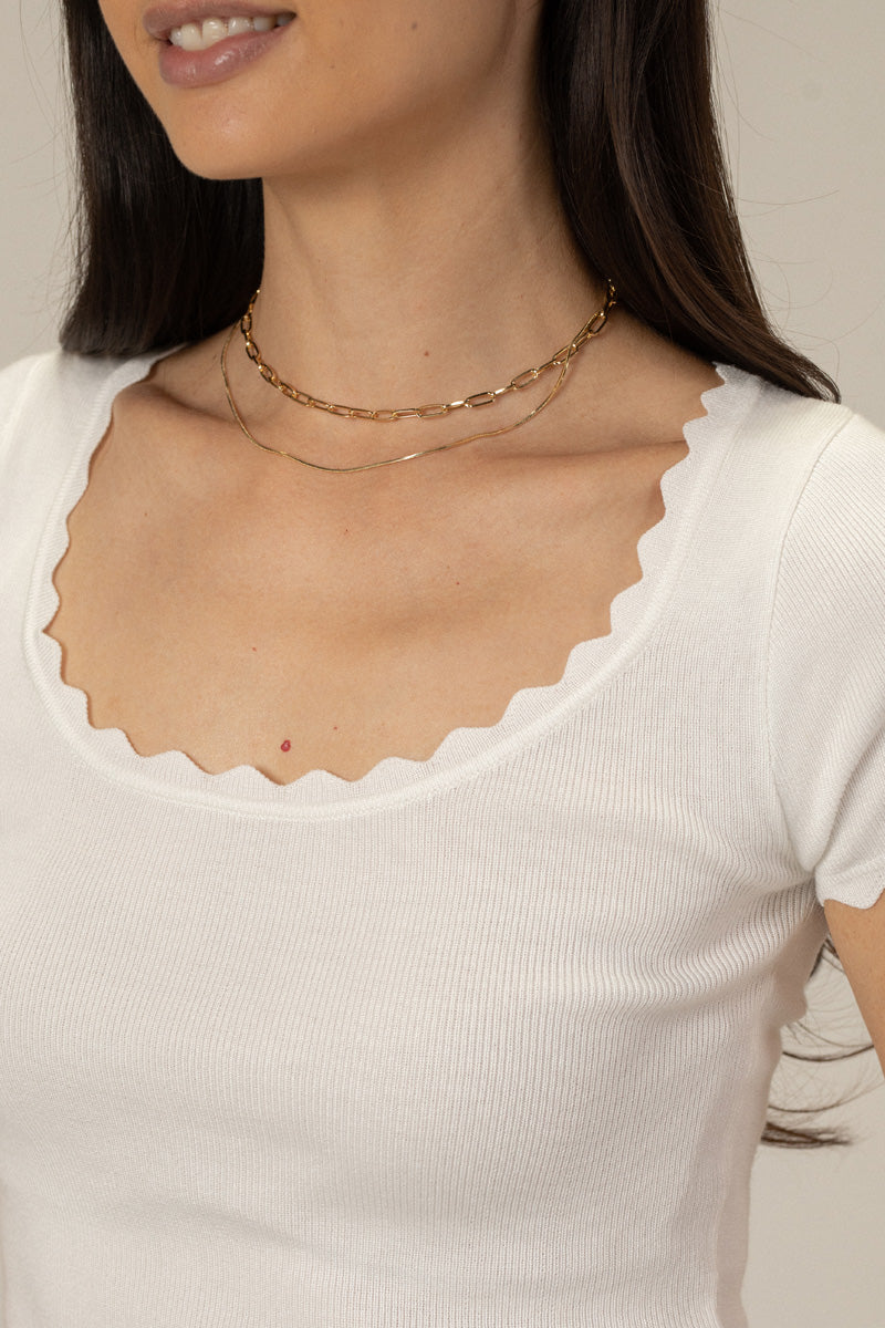 Layered gold chain necklace with delicate links, worn by a person with long dark hair against a white background.