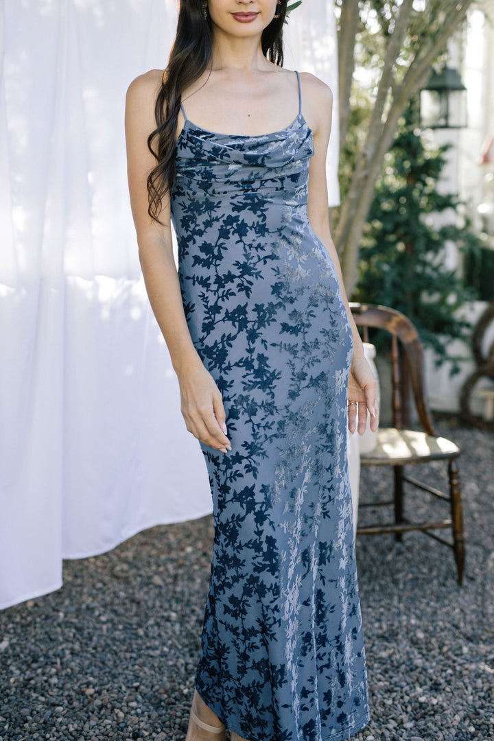 A sleeveless blue floral velvet dress with a cowl neckline and form-fitting silhouette.