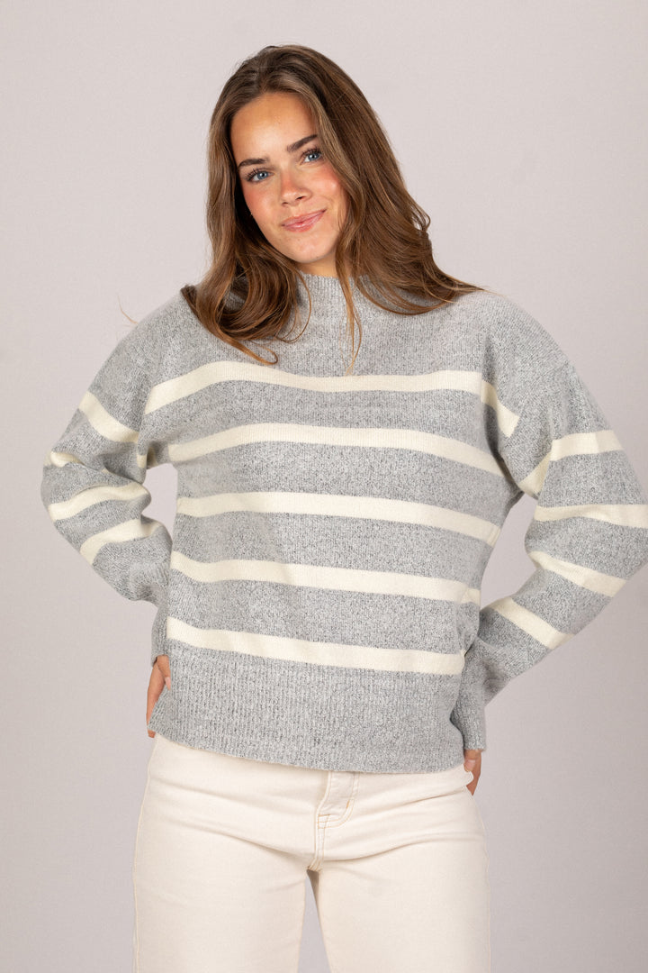 A gray and ivory striped knit sweater with a high collar and flared sleeves, modeled by a woman with long brown hair.