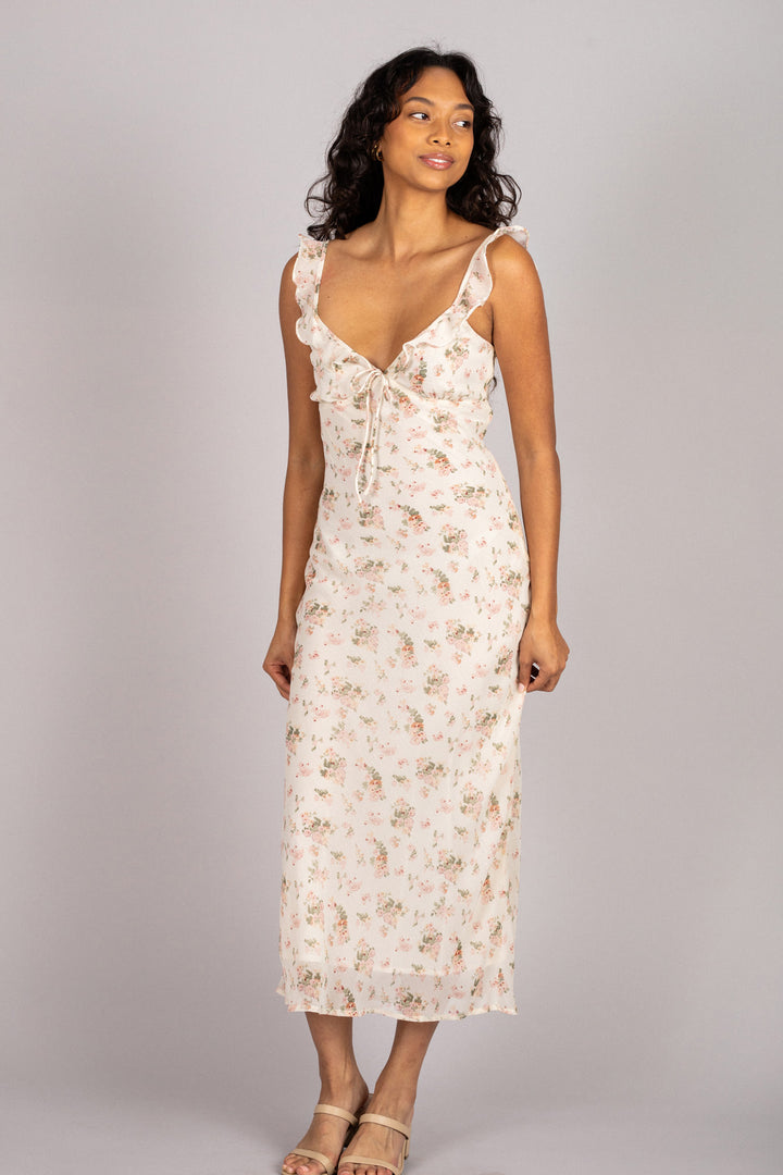 A floral-printed chiffon dress with a v-neckline, ruffle trim, and a midi-length hem, worn by a woman with long curly hair.