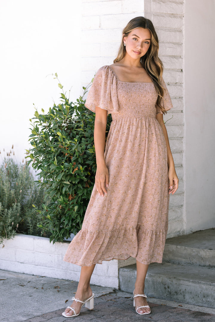 A smocked midi dress in a light pink floral print, with puff sleeves, a fitted waist, and a flowing, tiered skirt.
