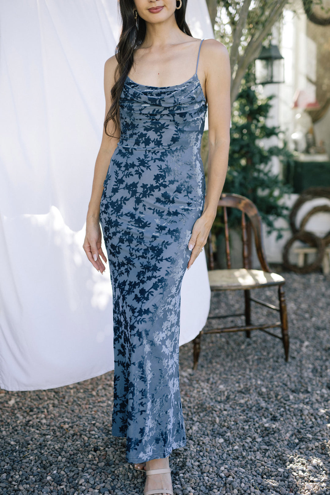 A form-fitting sleeveless dress in a blue floral velvet print, with a cowl neckline and a long maxi length silhouette.