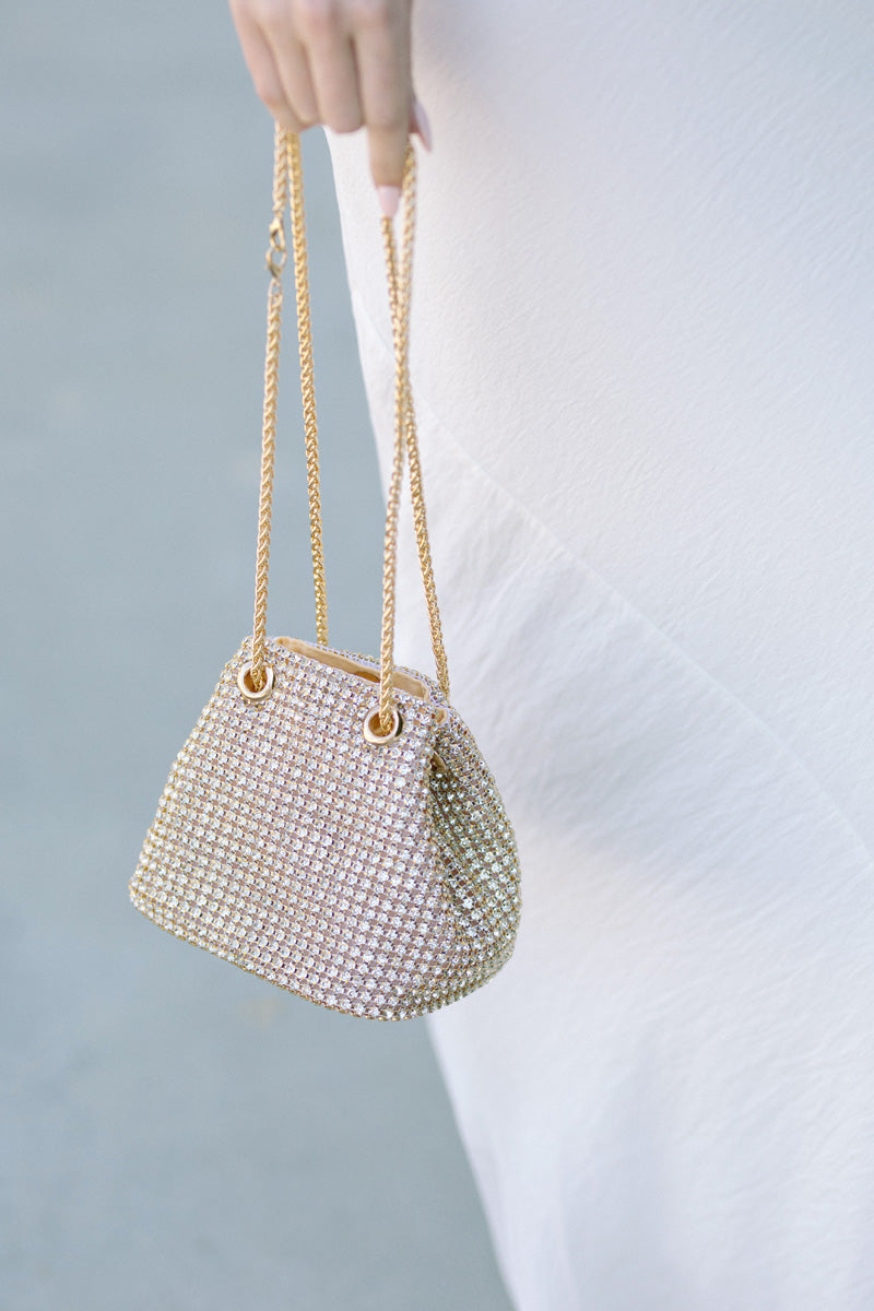 Glitzy gold-toned bucket bag covered in shimmering rhinestones, with a magnetic closure and long chains.
