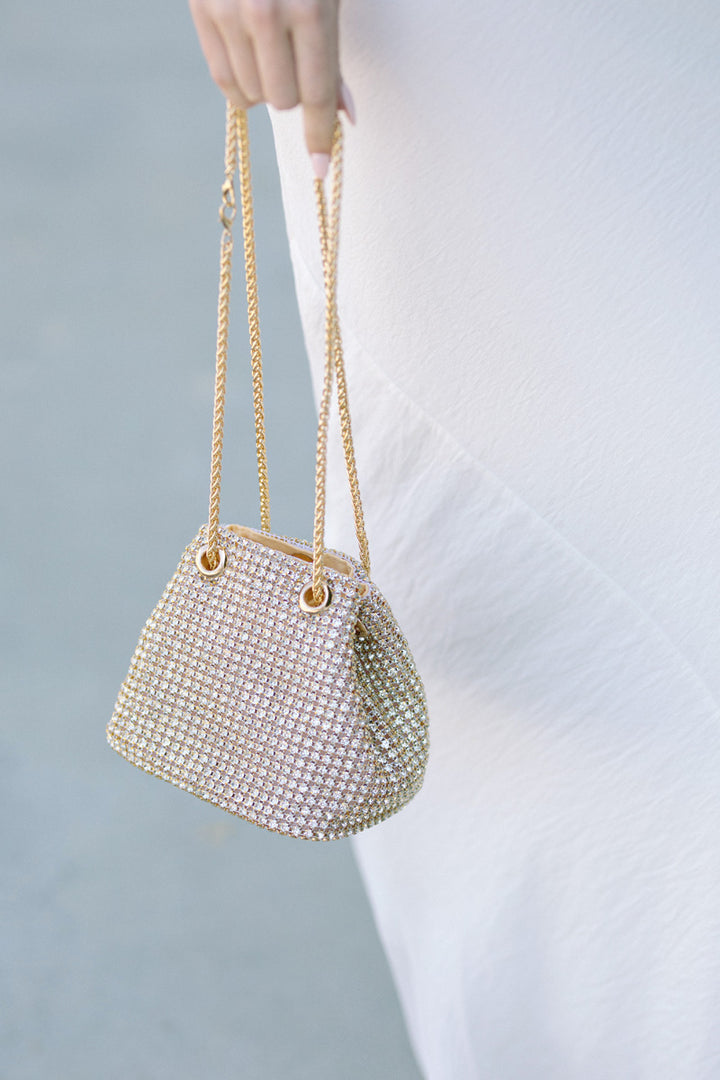 Glitzy gold-toned bucket bag covered in shimmering rhinestones, with a magnetic closure and long chains.