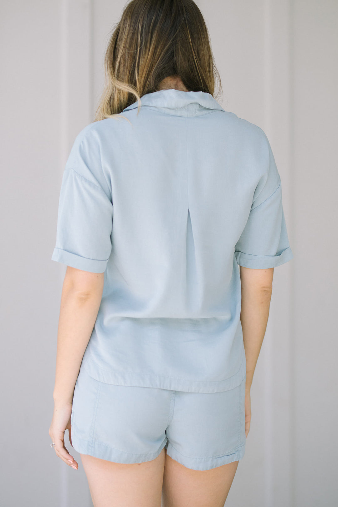 Light blue button-down top with short sleeves and a collar, featuring a casual, relaxed style.
