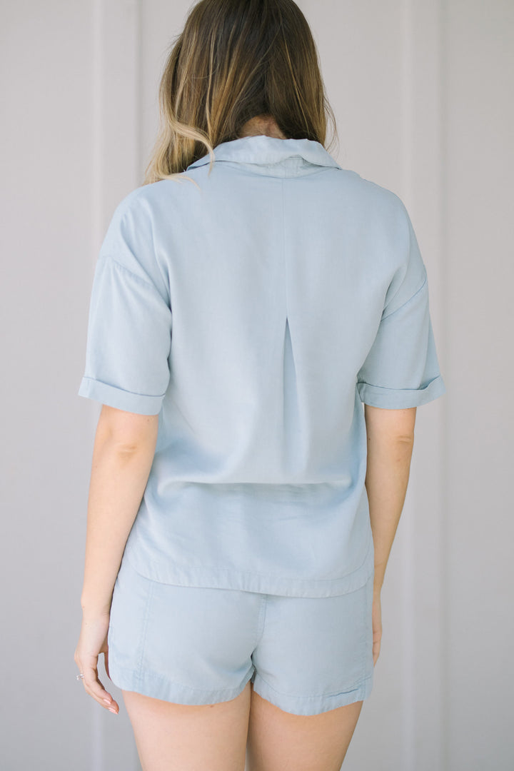 Light blue button-down top with short sleeves and a collar, featuring a casual, relaxed style.