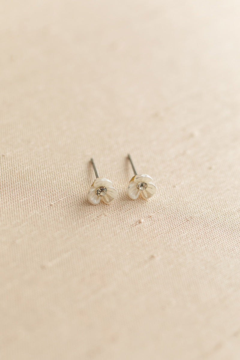 Two small silver flower-shaped earrings on a beige fabric background.