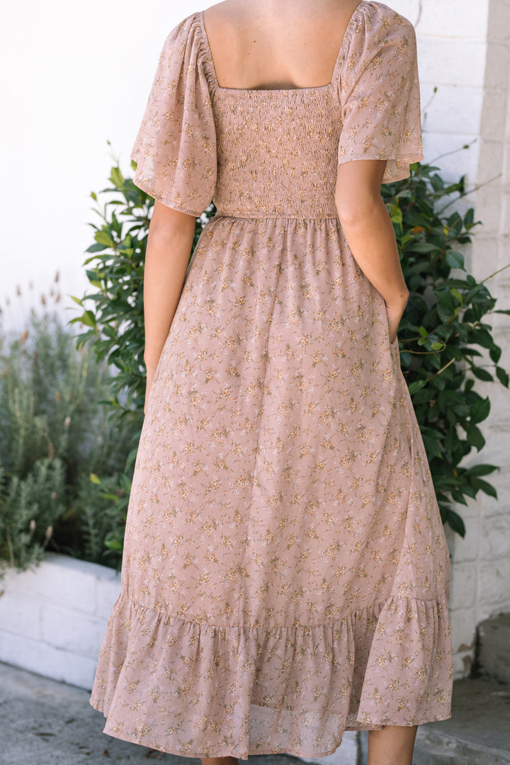 A floral patterned midi dress with a smocked bodice, puff sleeves, and a ruffled hem in a soft pink color.