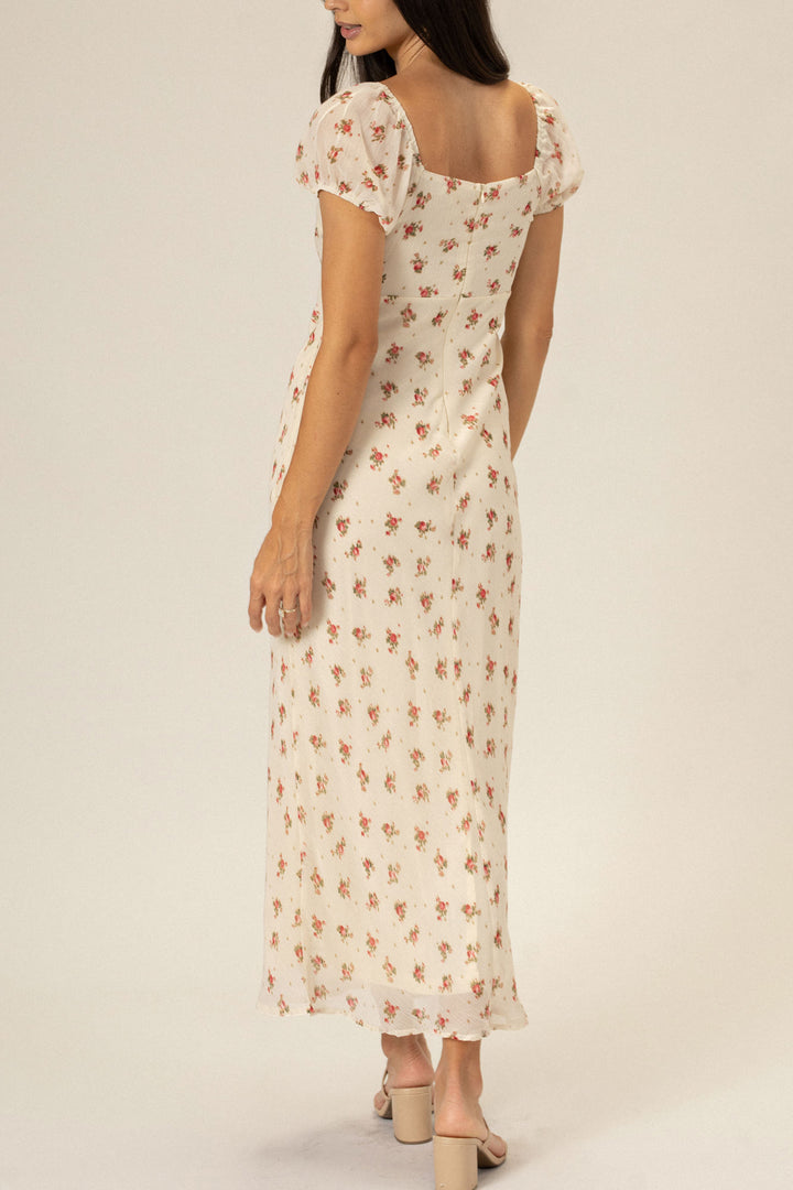 A white floral-printed maxi dress with puff sleeves, a v-neckline, and a flowing skirt.