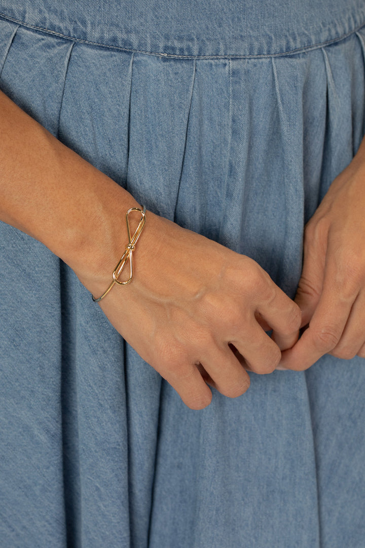 A gold metal bow-shaped bracelet against a denim background, showcasing the simple yet elegant design.