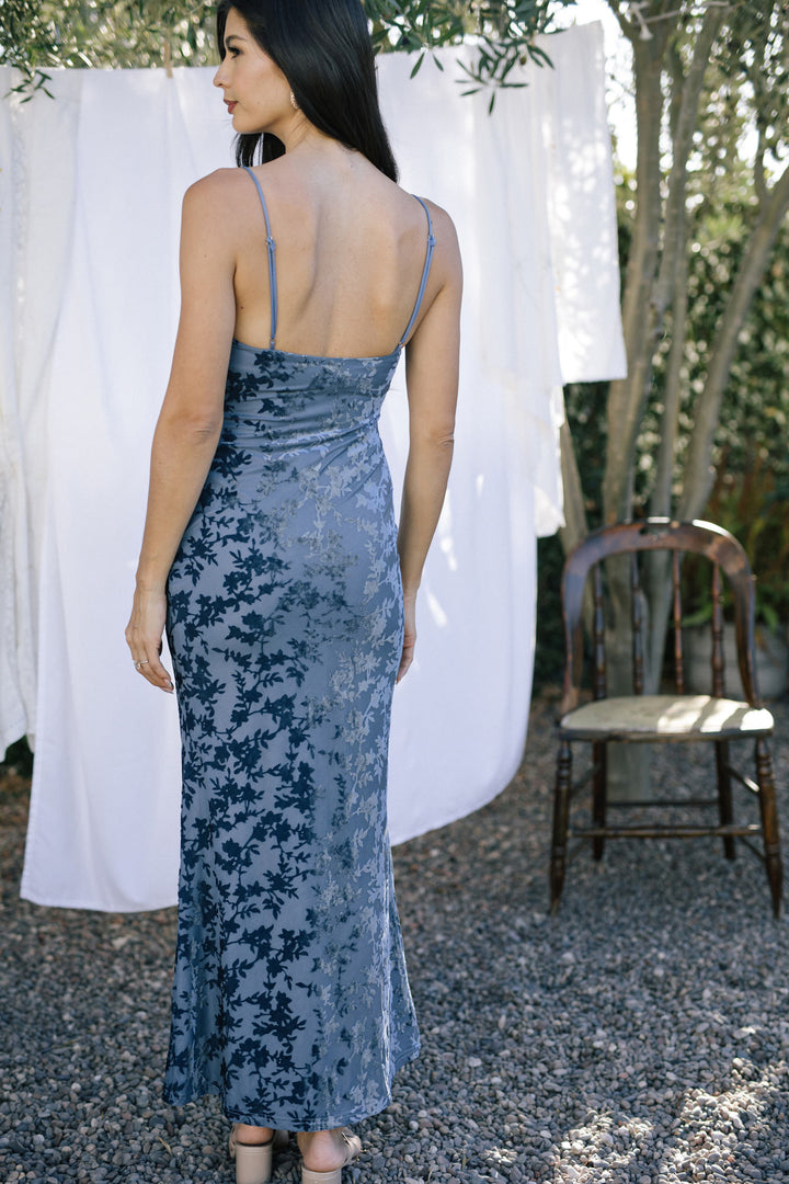 A sleeveless floor-length dress in a navy floral velvet pattern, with a plunging neckline and spaghetti straps.