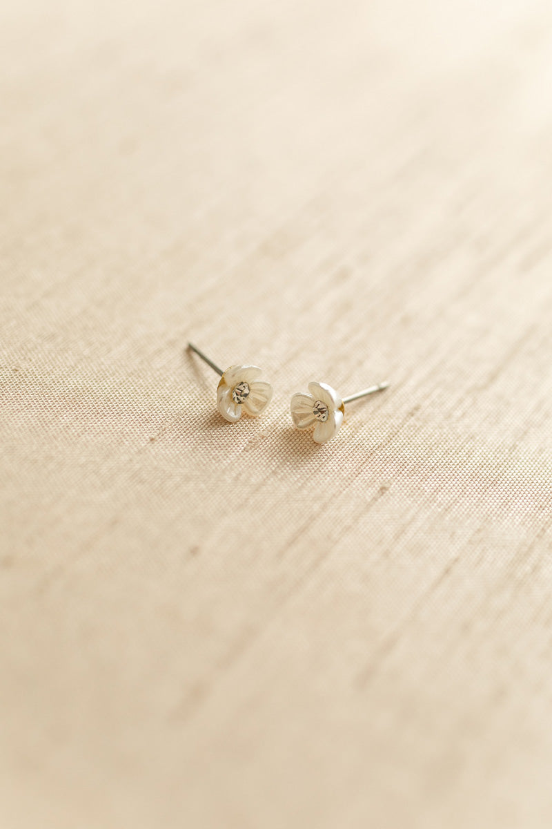 Two miniature silver floral stud earrings on a textured beige background.