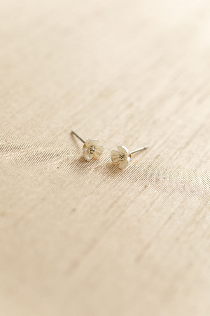 Two miniature silver floral stud earrings on a textured beige background.