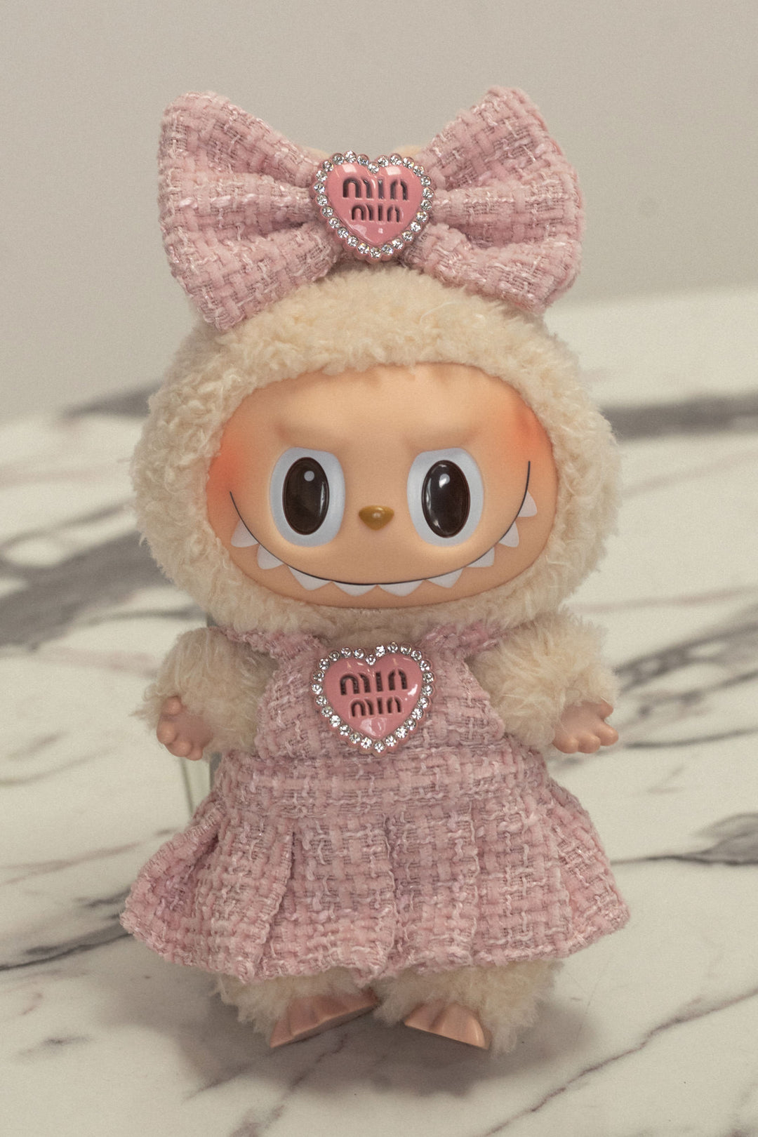 Plush pink toy in tweed dress with bow, heart emblem, and large eyes