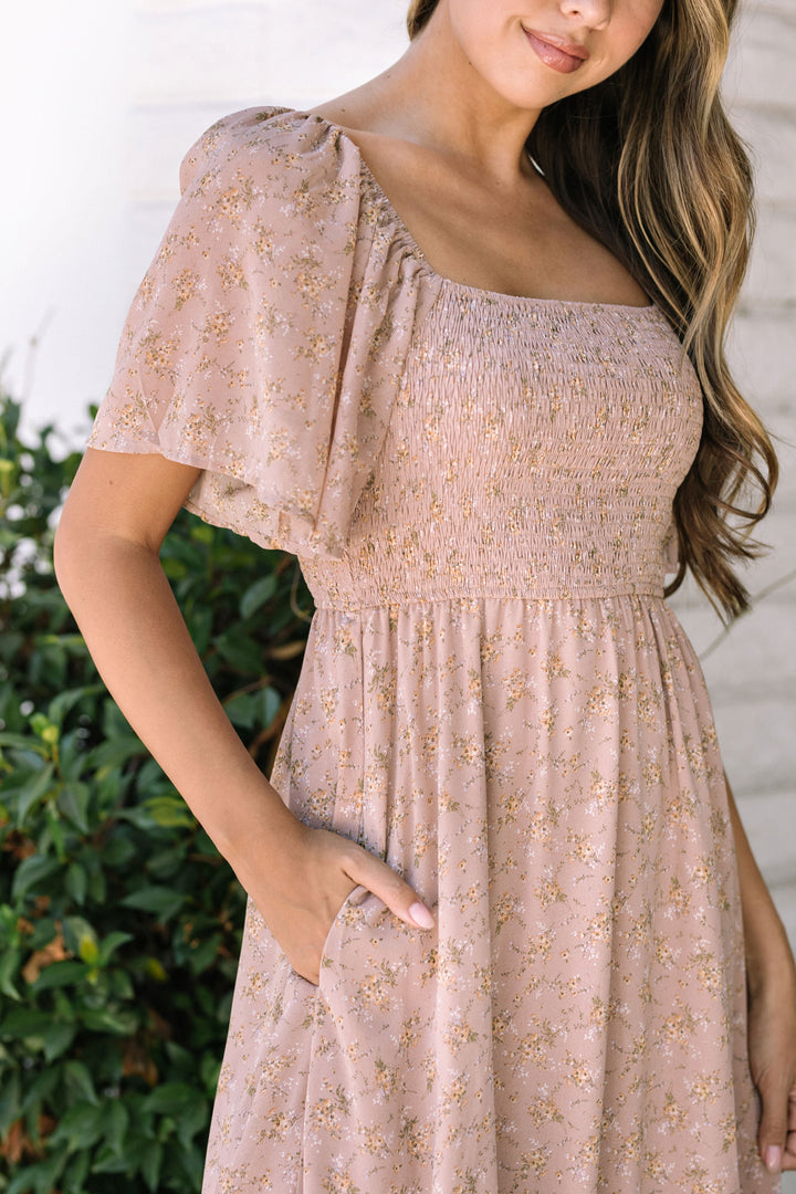 A pink floral midi dress with puffed off-the-shoulder sleeves, a smocked bodice, and a flowing skirt.
