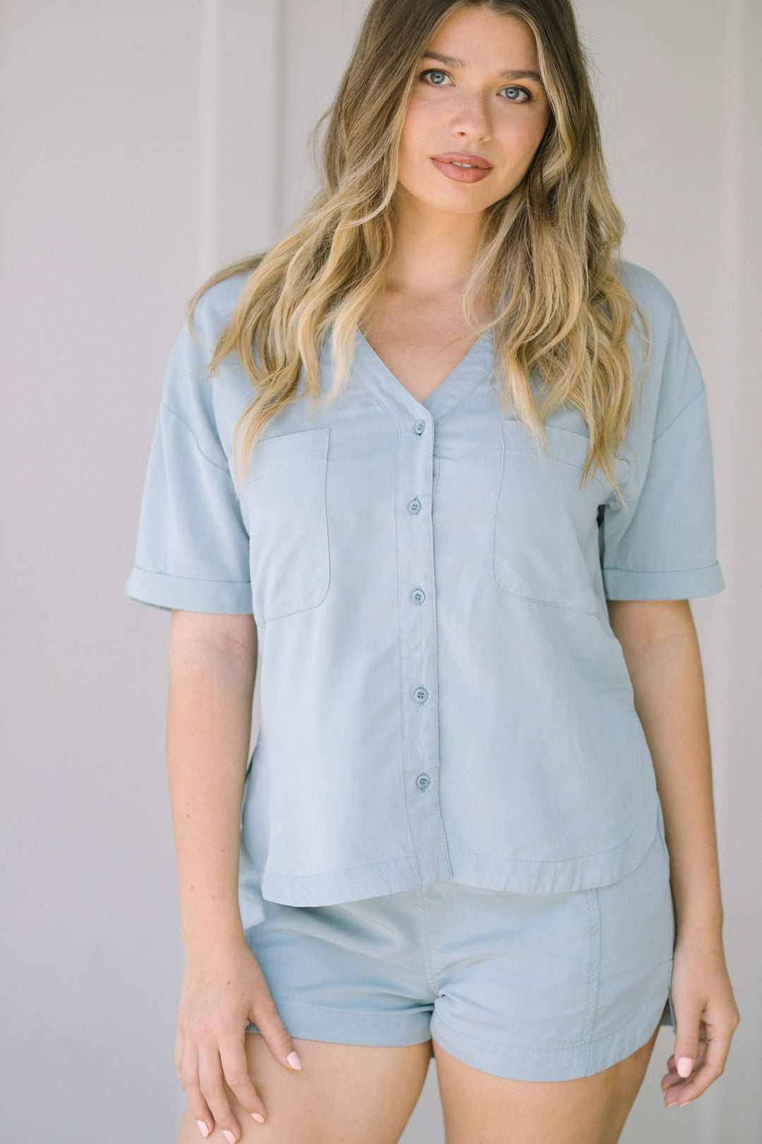 Light blue button-up shirt with rolled sleeves, paired with matching light blue high-waisted shorts, creating a casual and trendy summer look.