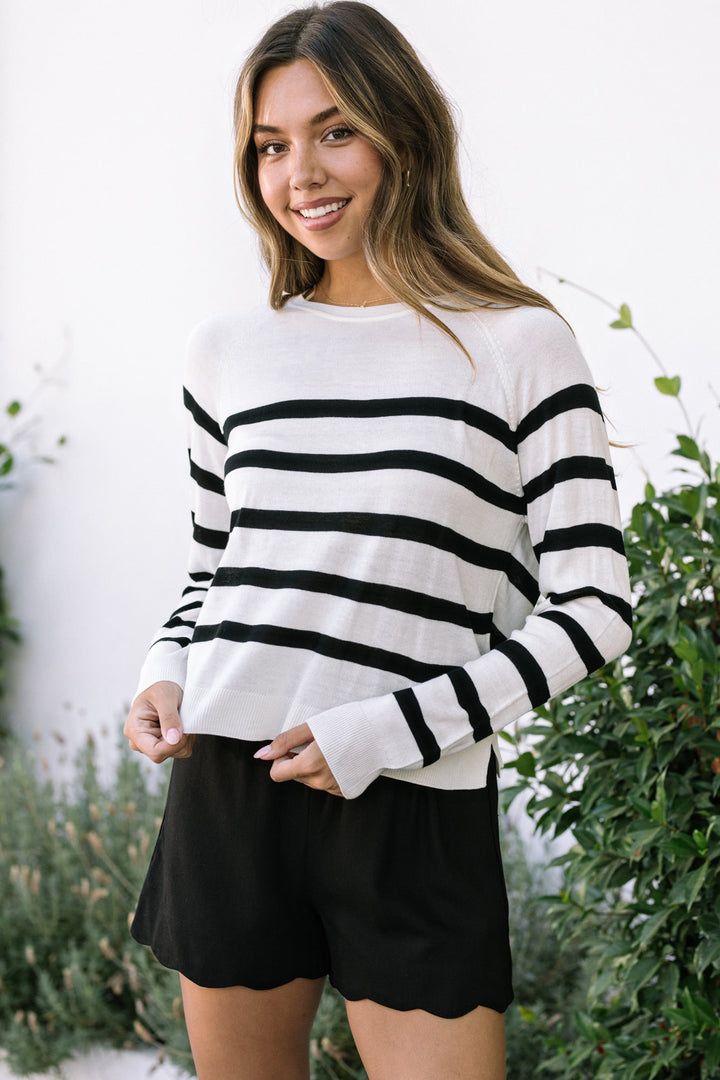 White and black striped sweater with long sleeves, paired with black scalloped shorts, worn by a smiling young woman outdoors.