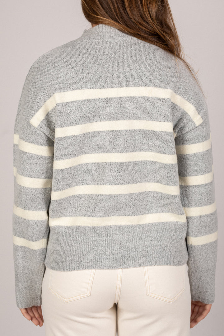A grey and white striped knit sweater with a high neckline and ribbed cuffs and hem, showcased on a female model.