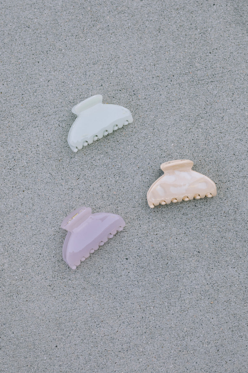 Three colorful plastic claw hair clips in white, pink, and lavender shades with subtle textured detailing.