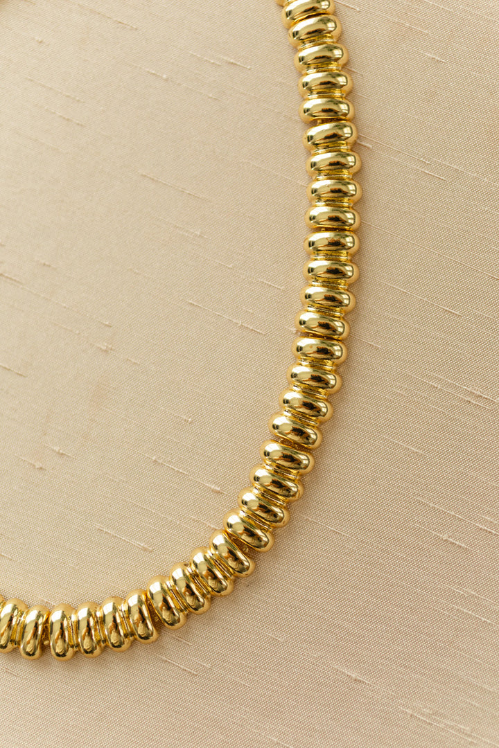A golden necklace with a textured, disc-shaped design, providing an elegant and modern accessory.