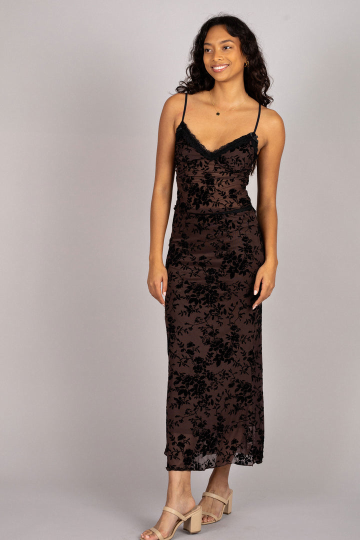 A dark brown maxi dress with a floral burnout pattern, featuring spaghetti straps and a figure-flattering silhouette.