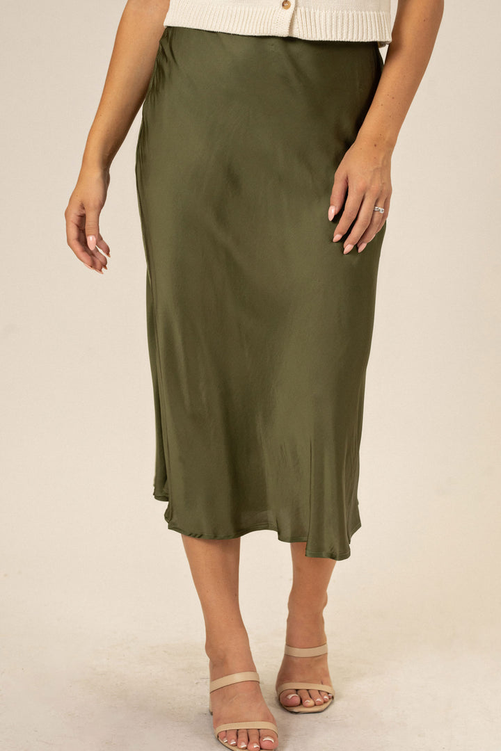 A long olive green slip skirt with a flared hemline, worn by a model with a sleek silhouette.
