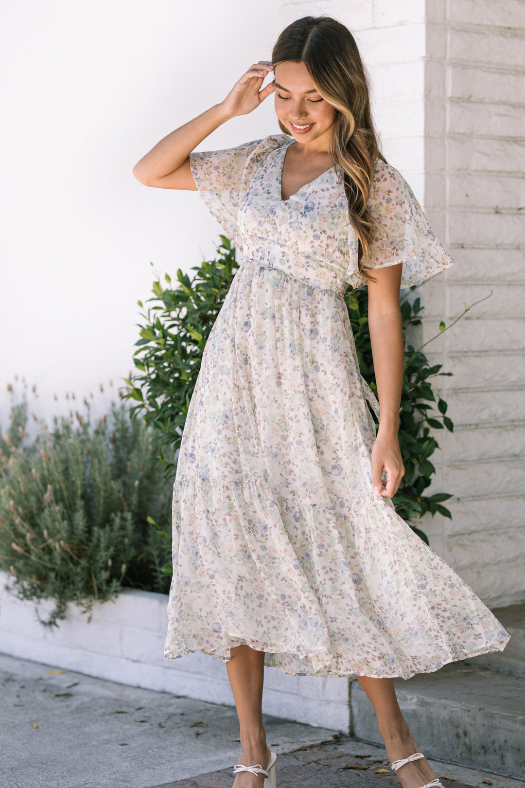 A floral print midi dress with flutter sleeves, cinched waist, and flowing, tiered skirt.