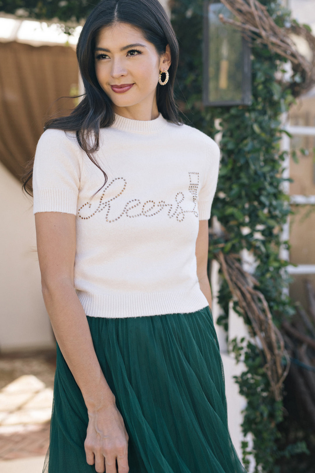 White knit sweater with rhinestone "Cheers" text and green pleated midi skirt, modeled by a young Asian woman with dark hair.