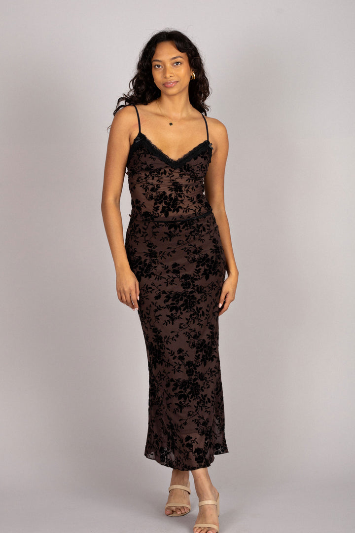 A woman wearing a sleeveless black floral burnout maxi dress with a plunging neckline and spaghetti straps.