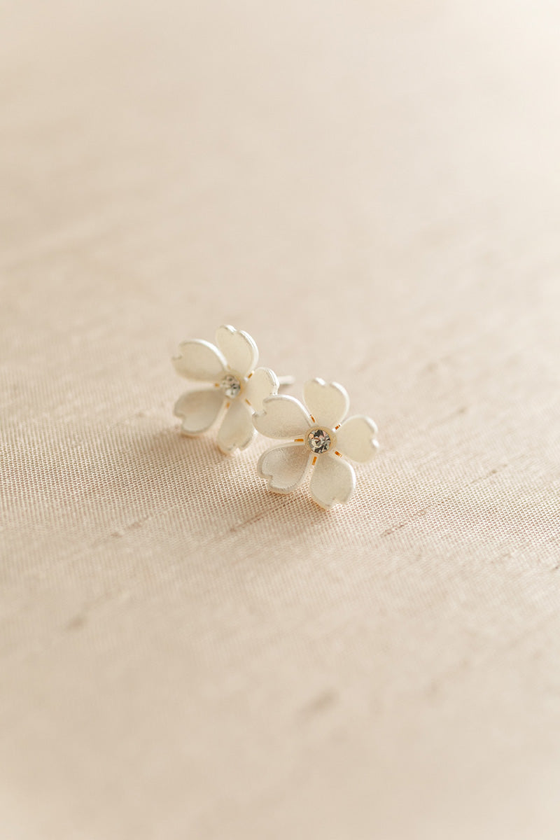 Two delicate white flower earrings with glittering centers, resting on a soft beige background.
