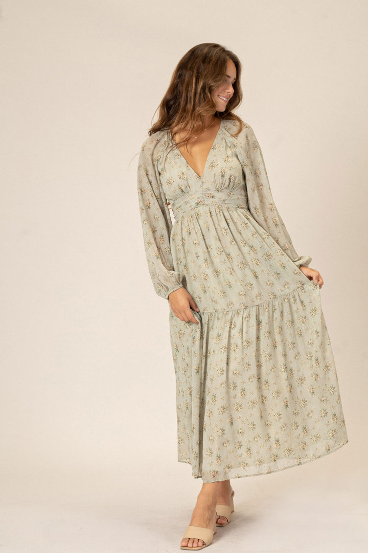 A long-sleeved maxi dress in a light, floral-patterned fabric with a deep V-neckline, high waistline, and tiered skirt.