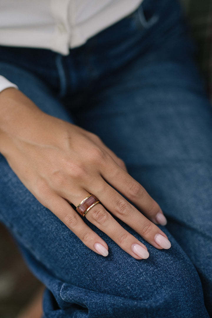 Close-up of a hand wearing a ring set consisting of a gold band and a burgundy stone ring on the person's fingers.