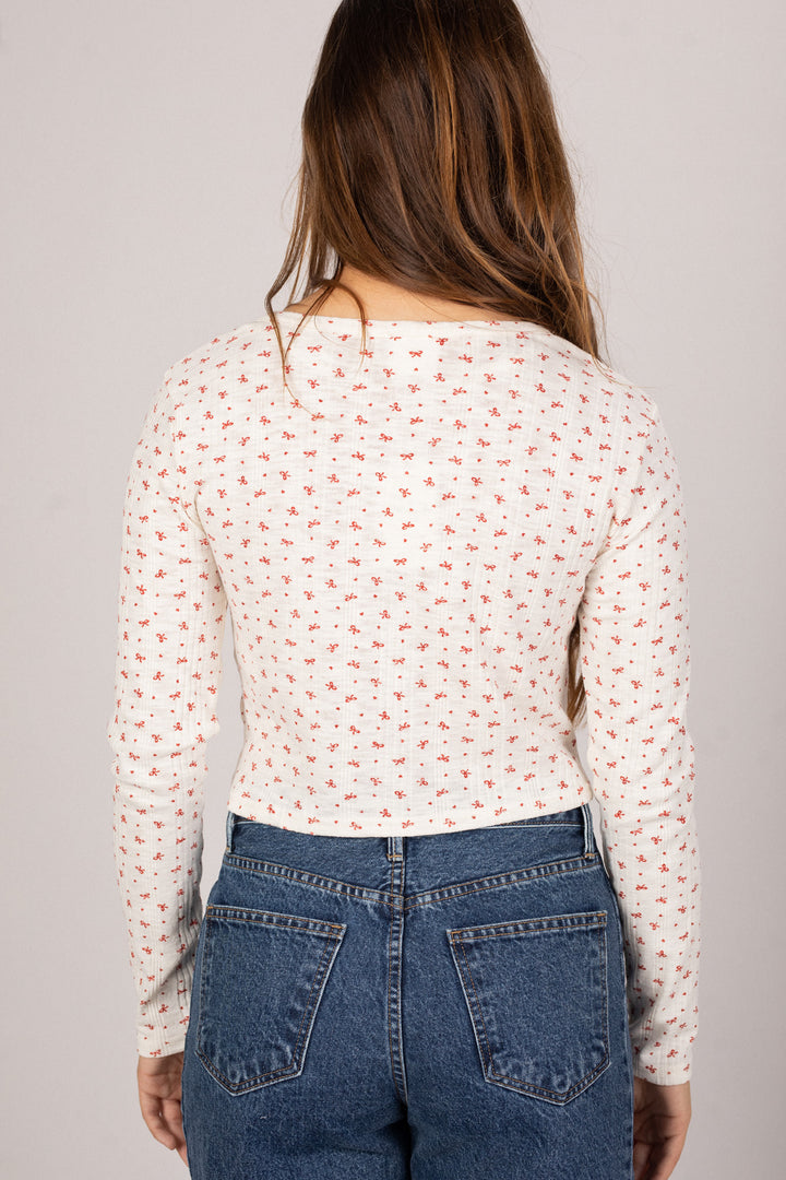 Close-up of a woman's back wearing a long-sleeved, buttoned knit top with a small red floral pattern on a white background.