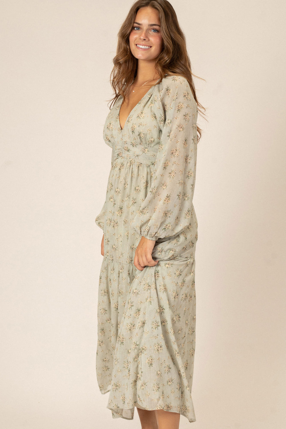 A long-sleeved midi dress in a soft beige floral print, with a v-neckline and billowing sleeves, showcasing a feminine, romantic style.