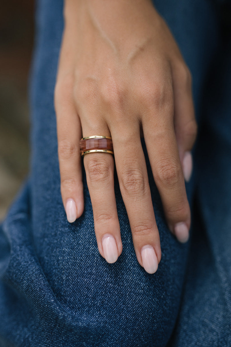 Close-up of a hand wearing a gold and maroon ring set against a denim background.