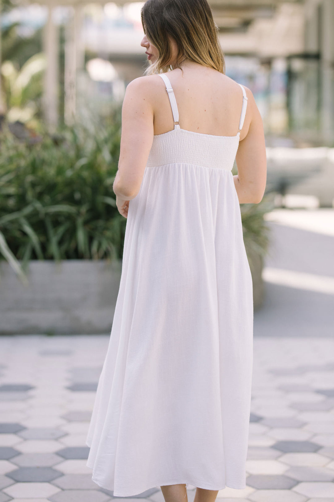 A flowing, white linen-blend midi dress with a cinched waist and spaghetti straps, creating a relaxed, feminine silhouette.
