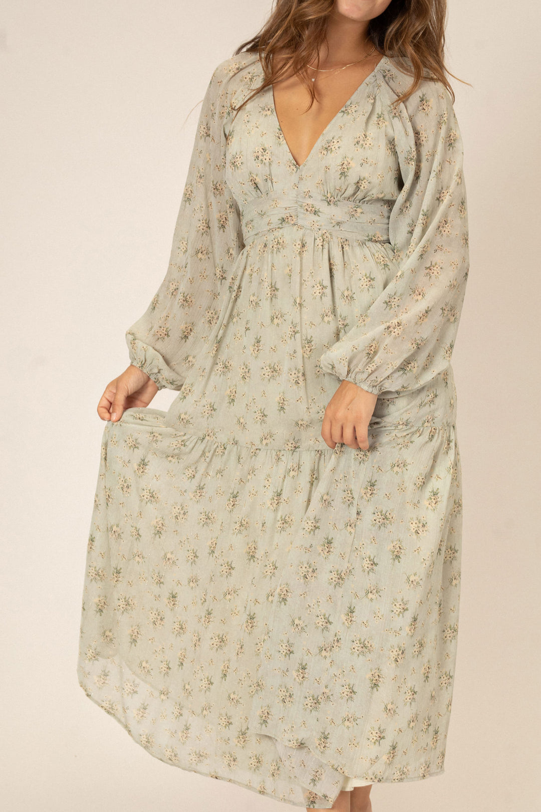 Flowing floral-printed midi dress with long billowy sleeves, V-neckline, and ruffled hem in a soft beige tone.