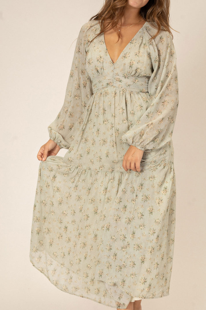 Flowing floral-printed midi dress with long billowy sleeves, V-neckline, and ruffled hem in a soft beige tone.