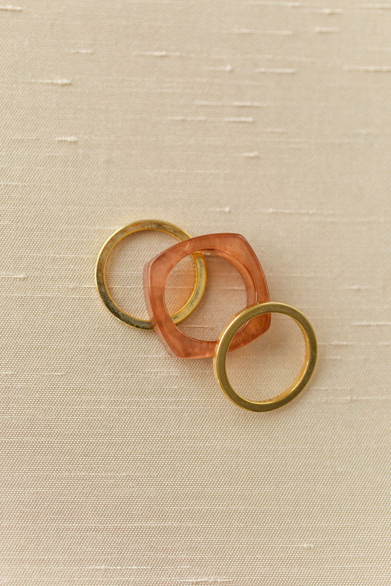 Three stacking rings in gold and peach tones, featuring a unique sculptural design.