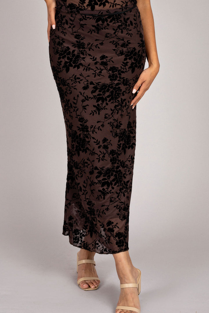 A brown floor-length skirt featuring a flowing floral burnout print, designed for a graceful and feminine look.