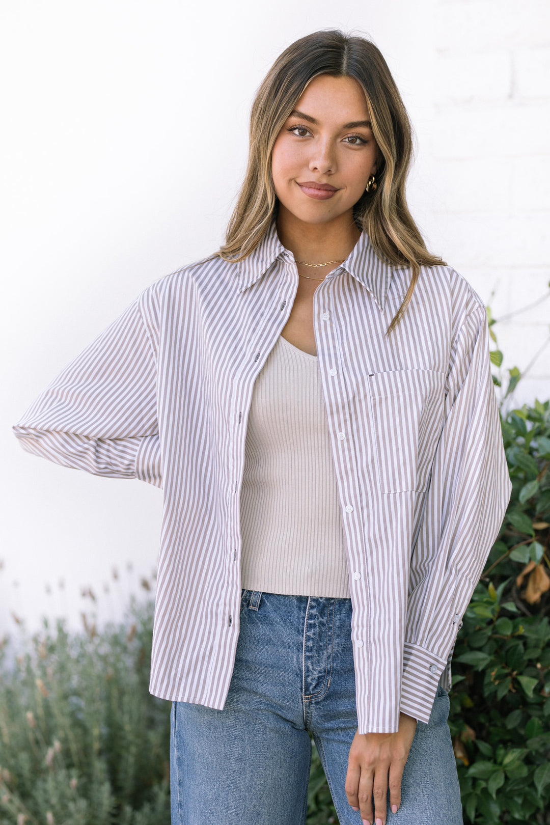 A woman wearing a striped button-up shirt in a relaxed, casual style with a collared neckline and pockets on the front.
