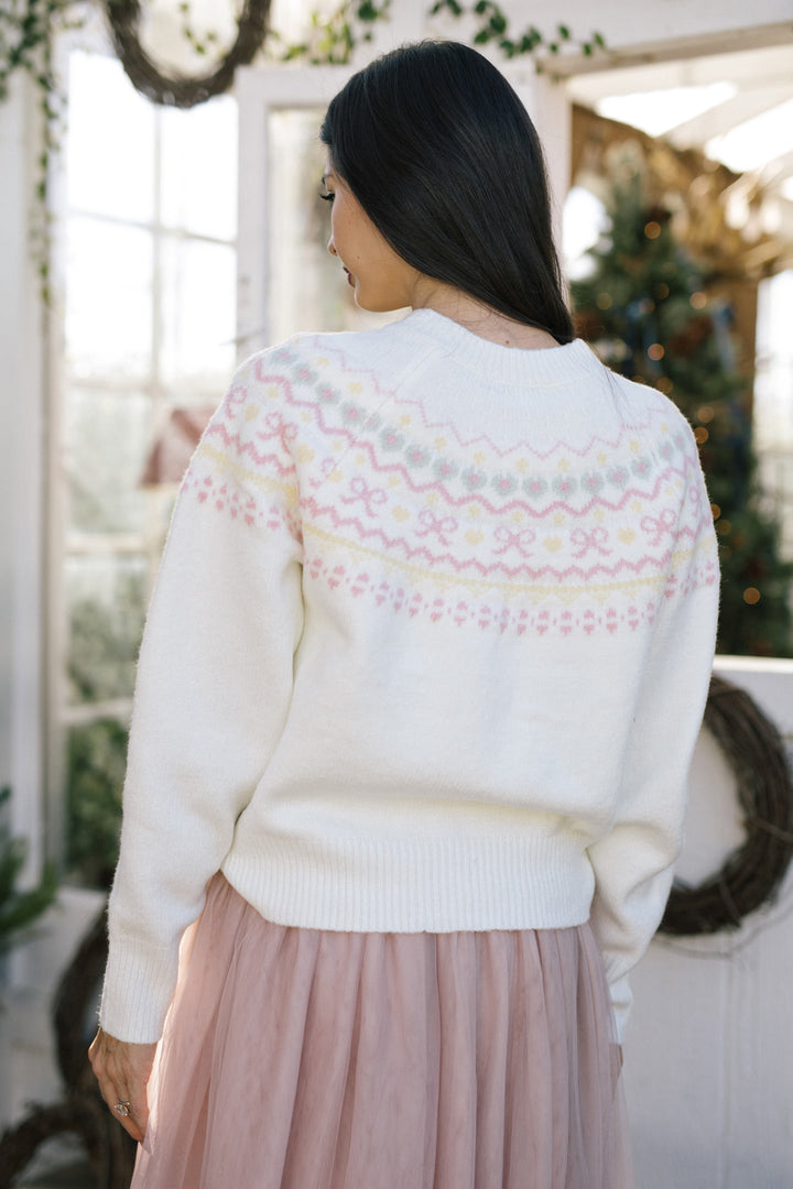 A woman wearing a white knit cardigan with a delicate pink and yellow geometric pattern on the back, paired with a pink tulle skirt.