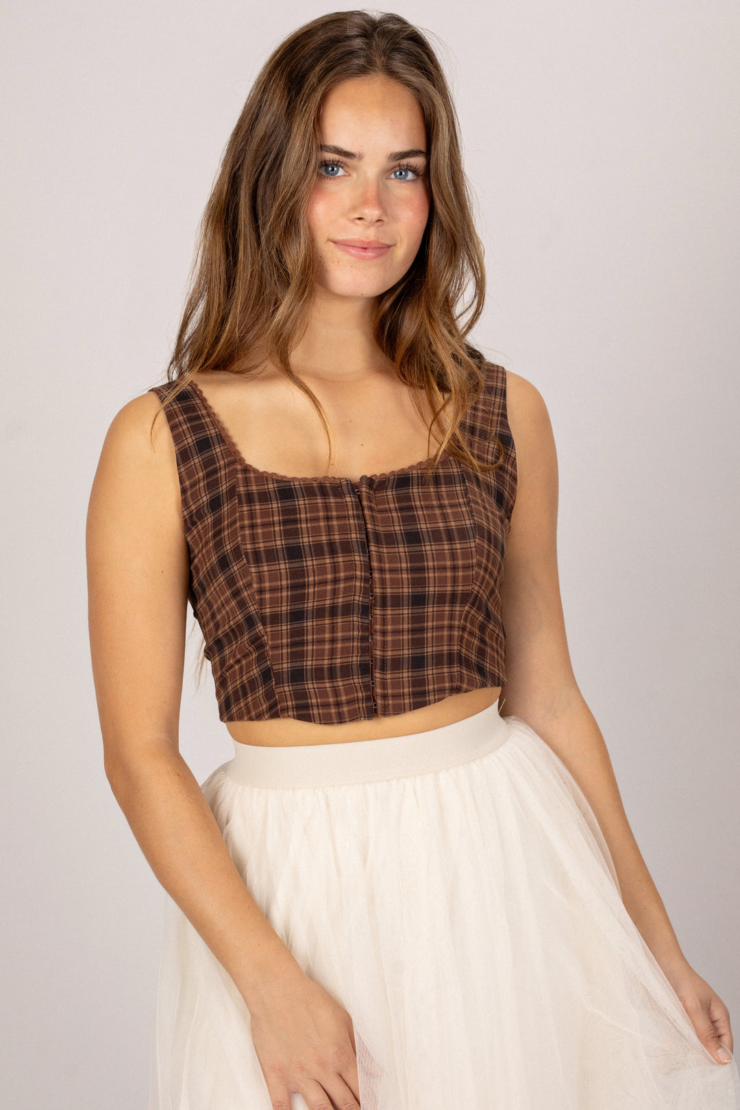 A young woman with long brown hair wearing a plaid cropped top and a white tulle skirt.